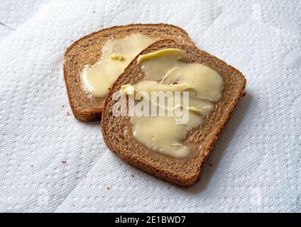 Vista dall'alto di due fette di pane di grano leggermente tostato con margarina su asciugamani di carta bianca con luce naturale. Foto Stock