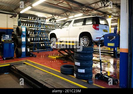 Riparazione e sostituzione di pneumatici e scarico del veicolo Kwik Fit macchina bianca con ruota anteriore rimossa per la riparazione della foratura Foto Stock