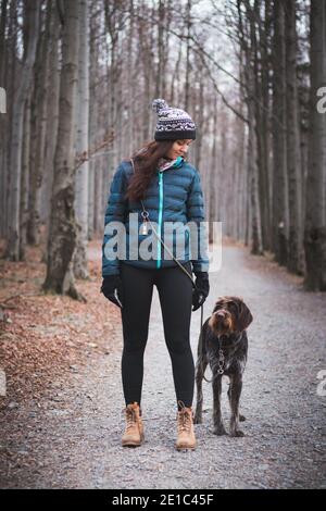 Giovane donna con il suo cane in bella foresta in una passeggiata mattutina. Collegamento tra un cane e una donna. Rapporto di fiducia reciproca. Donna con jacke blu Foto Stock