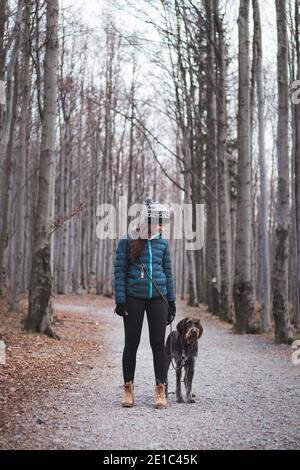 Giovane donna con il suo cane in bella foresta in una passeggiata mattutina. Collegamento tra un cane e una donna. Rapporto di fiducia reciproca. Donna con jacke blu Foto Stock