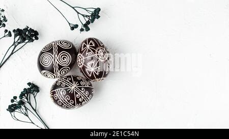 Uova di Pasqua nere fatte a mano. Pysanka Ucraina decorata con tecnica di tintura cerata-resistente. Sfondo bianco con spazio vuoto per la copia del testo Foto Stock