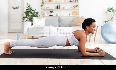 Allenamento domestico. Donna nera che si allenano sul tappeto yoga, facendo la posizione del gomito, rinforzando i muscoli abs Foto Stock