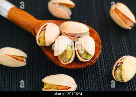 Pistacchi in cucchiaio di legno su tovagliolo nero. Primo piano Foto Stock