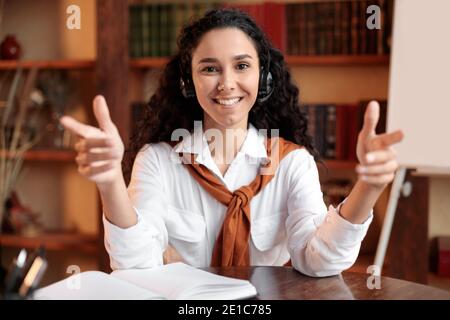 Donna seduta alla scrivania, che parla con la fotocamera indossando la cuffia Foto Stock