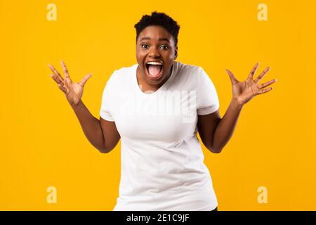 Più-dimensione African Woman Screaming in eccitazione che posa su sfondo giallo Foto Stock