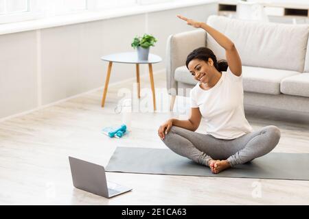 Donna nera sportiva che si esercita a casa guardando tutorial sul computer portatile Foto Stock