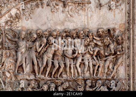 Un angelo vendicativo guida i dannati verso i demoni pelosi trascinandoli all'inferno con un bassorilievo in marmo del giudizio universale degli anni '1300 sul fronte occidentale della cattedrale di Orvieto, in Umbria, Italia. Questa scena scolpita è attribuita a Lorenzo Maitani (c. 1275 - 1330), che progettò la facciata tardo gotica della cattedrale. Si ritiene che Maitani abbia avuto un contributo diretto come scultore su due pannelli che coprono due delle quattro pilastri inferiori della facciata: Un pannello Maitani raffigura scene del giudizio universale, compresa la scena in questa immagine. Foto Stock