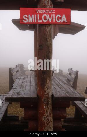 Punto di osservazione Smilovica, con cartello rosso, panchine e tavoli in legno, in una giornata nebbiosa e nebbiosa Foto Stock