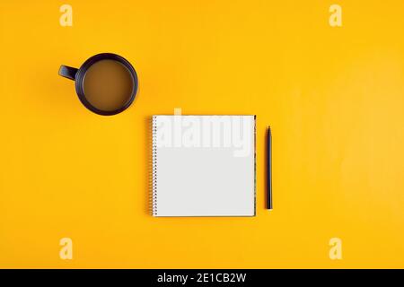 Blocco note o blocco note vuoto con penna e tazza di caffè su sfondo giallo. Foto Stock