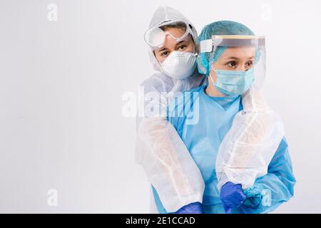 I medici stanchi in tute protettive sono abbracciati e sostenuti guardando al lato. Supporto in tempi difficili. Spazio laterale. Foto Stock