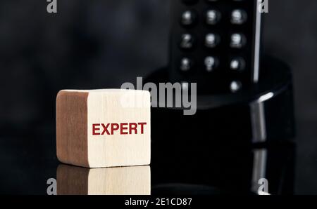 La parola esperto su blocco di legno con sfondo telefono. Chiedere il concetto di consiglio di un esperto. Foto Stock