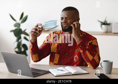 Uomo africano dispiaciuto che prende la maschera al lavoro per Scratch Barba Foto Stock