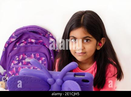 Una bambina con auricolari e tablet che prende lezioni online durante la pandemia di covid. Concetto di e-learning. Foto Stock