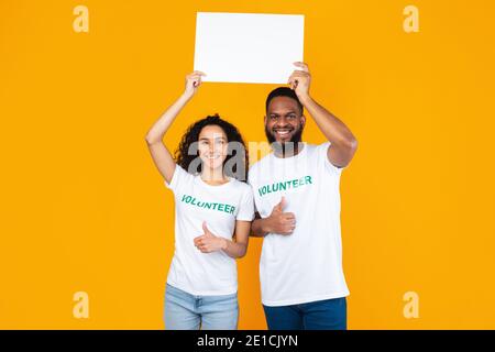 Volontarii che tiene la scheda di carta sopra la testa che gestura Thumbs-Up, sfondo giallo Foto Stock