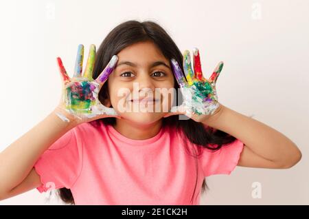 Ritratto di una felice e sorridente bambina indiana che gioca e si gode con le pitture nelle dita. Foto Stock