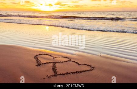 Il giorno di San Valentino di sunny beach. Due cuori attirato in sabbia, concetto di amore Foto Stock