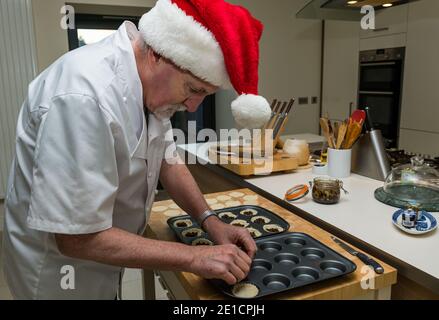 Uomo anziano che indossa bianco chef e cappello di Santa che fa mince Torte al tempo di Natale in una cucina casalinga Foto Stock