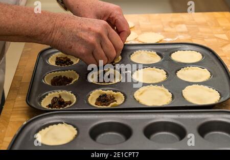 Mani dell'uomo che riempiono le casse di pasta in tini da forno con la carne macellata Per fare torte mince al tempo di Natale Foto Stock