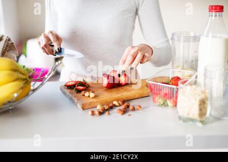 Le fragole fresche appena fuori dal giardino vengono tagliate da una donna su una luminosa scrivania da cucina. Foto Stock