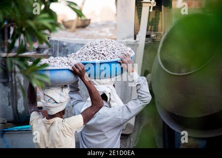 zoomed in colpo di operai di costruzione underprived indiani che trasportano la sabbia, il cemento, le pietre e l'acqua sulla loro testa per caricare in un miscelatore per fare Foto Stock