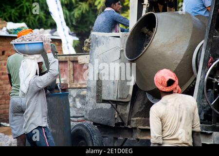 zoomed in colpo di operai di costruzione underprived indiani che trasportano la sabbia, il cemento, le pietre e l'acqua sulla loro testa per caricare in un miscelatore per fare Foto Stock