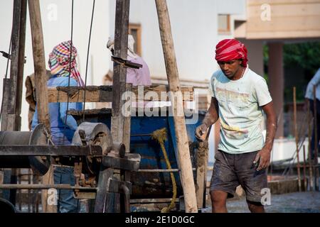 zoomed in colpo di operai di costruzione underprived indiani che trasportano la sabbia, il cemento, le pietre e l'acqua sulla loro testa per caricare in un miscelatore per fare Foto Stock
