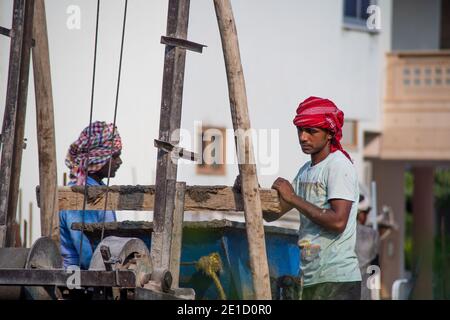 zoomed in colpo di operai di costruzione underprived indiani che trasportano la sabbia, il cemento, le pietre e l'acqua sulla loro testa per caricare in un miscelatore per fare Foto Stock