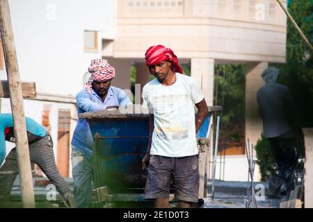 zoomed in colpo di operai di costruzione underprived indiani che trasportano la sabbia, il cemento, le pietre e l'acqua sulla loro testa per caricare in un miscelatore per fare Foto Stock