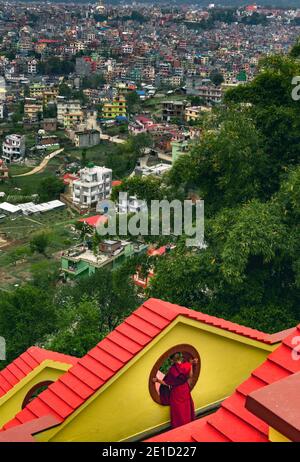 Un monaco giovane si affaccia sulla città di Kathmandu da un balcone al Monastero di Kopan Foto Stock