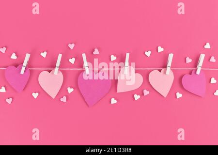 San Valentino con cuori di carta rosa appesi alla linea con i pioli e lo zucchero spruzzano Foto Stock