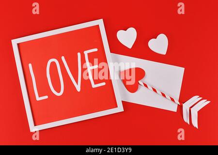 Composizione di San Valentino con cornice con testo 'AMORE', frecce d'amore cupido, lettera, e cuori su sfondo rosso Foto Stock