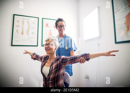 Bella infermiera professionista allegra che fa alcuni esercizi di fisioterapia con il paziente. Foto Stock