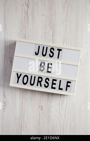 "Just be yourself" su un lightbox su una superficie di legno bianco, vista dall'alto. Posa piatta, sovratesta, dall'alto. Foto Stock