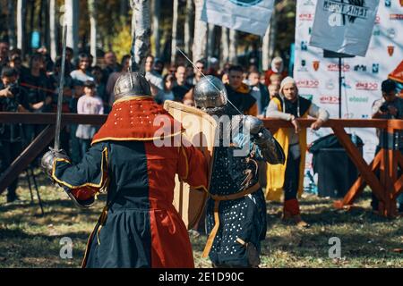 Ricostruzione di cavalieri nell'arena. Combatti di fronte al pubblico. Due cavalieri in armatura e con spade. Bishkek, Kirghizistan - 13 ottobre 2019 Foto Stock