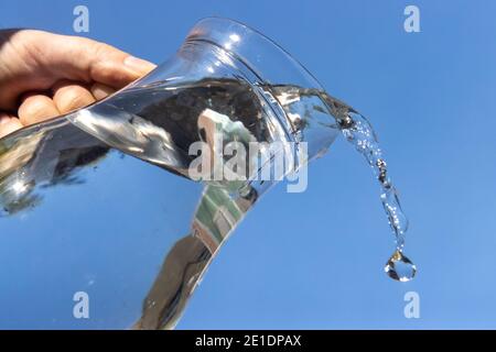 Un'acqua limpida che scorre da una caraffa di vetro su sfondo blu. Foto Stock