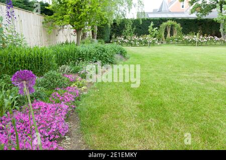 Ampio giardino all'inglese all'inizio dell'estate o in tarda primavera con fiori al confine e prato. Esempio di giardino paesaggistico design e giardinaggio, Regno Unito Foto Stock