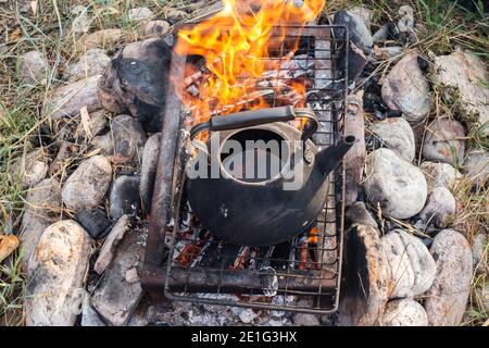 un bollitore con acqua calda sopra il fuoco. Teiera antica su pietre sulla griglia sopra il fuoco per la preparazione di tè o caffè outdoor.A speciale focolare per esterno. Foto Stock