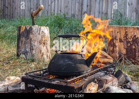 bollitore d'acqua calda sopra il fuoco. Antico bollitore su pietre su una griglia sopra un fuoco nel cortile di una casa di campagna. Tè o caffè. Foto Stock