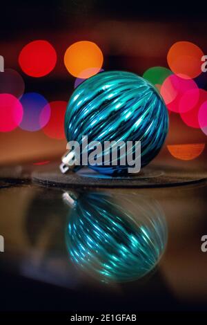 Una macro ripresa di un ornamento blu riflettente con colore luci dietro di esso Foto Stock