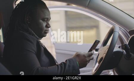 Uomo afroamericano riuscito che ottiene il messaggio di testo sorpreso mentre sedendosi sul sedile del conducente della sua automobile. Foto di alta qualità Foto Stock