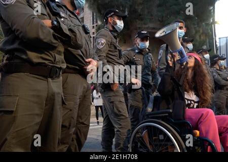 Un protestante in sedia a rotelle usa un corno mentre siede in mezzo alle forze di sicurezza israeliane al di fuori del composto della residenza ufficiale del primo ministro israeliano durante una manifestazione contro il primo ministro Benjamin Netanyahu per la sua accusa di corruzione a Gerusalemme, Israele Foto Stock