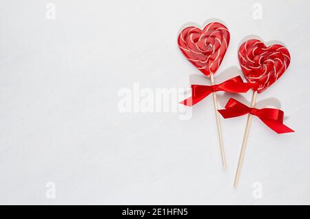 Cuori di lecca rossi con fiocco di seta su tavola di legno bianco come sfondo festivo di giorno di valentines. Foto Stock