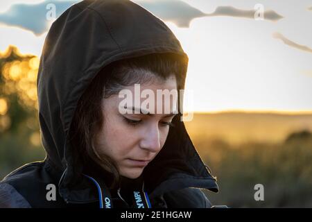 Bianca donna caucasica con la testa in giù. Sguardo triste e verso il suolo. Contro la luce in un tramonto Foto Stock