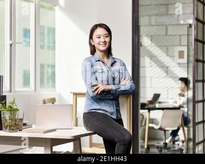 ritratto di una giovane donna asiatica d'affari che guarda la macchina fotografica sorridi le braccia incrociate Foto Stock