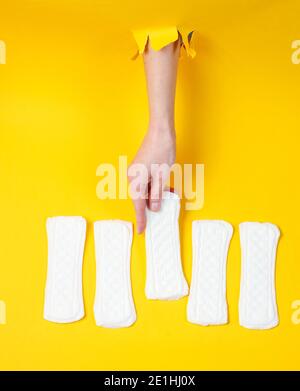 La mano femmina tiene il tampone sanitario quotidiano attraverso lo sfondo di carta giallo strappato. Concetto di moda minimalista Foto Stock