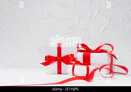 Scatole regalo bianche di diverse dimensioni con nastro di seta rossa in interni bianchi, spazio per la copia, sfondo per matrimoni. Foto Stock