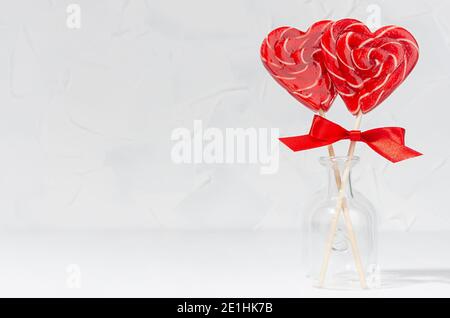 Cuori di lecca rossi con fiocco di seta in vaso di vetro in bianco interno come valentines festivo sfondo giorno. Foto Stock