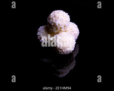 Caramella bianca rotonda con fiocchi di cocco su sfondo nero. Caramella al cioccolato. Cioccolato bianco. Fiocchi di cocco. Gelato bianco rotondo. Gelato Foto Stock