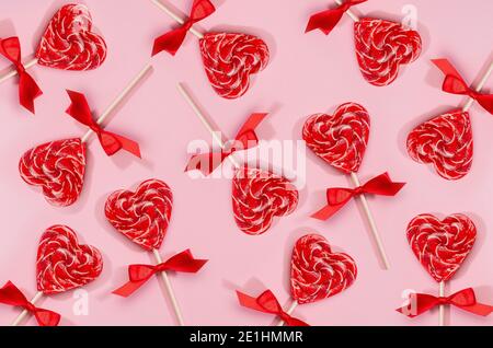 Cuori di lecca rossi con arco di seta patten su rosa pastello come sfondo festivo del giorno di San Valentino. Foto Stock