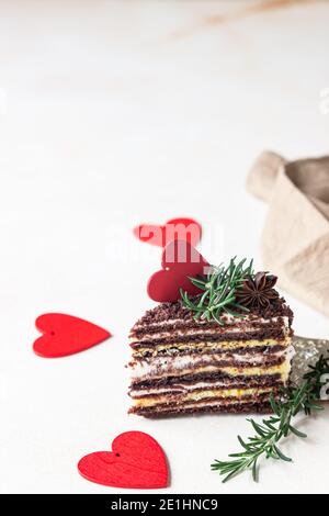 Il pezzo di torta stratificata di cioccolato e cuori rossi su fondo di cemento chiaro. Decorazioni festive per il giorno di San Valentino. Torta di miele russa, Medovik. Selettivo Foto Stock